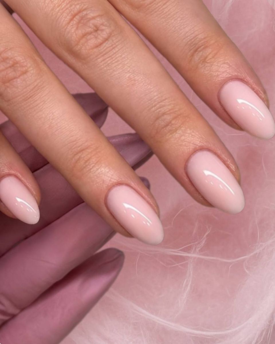 Soft blush almond manicure resting against airy rose-pink texture