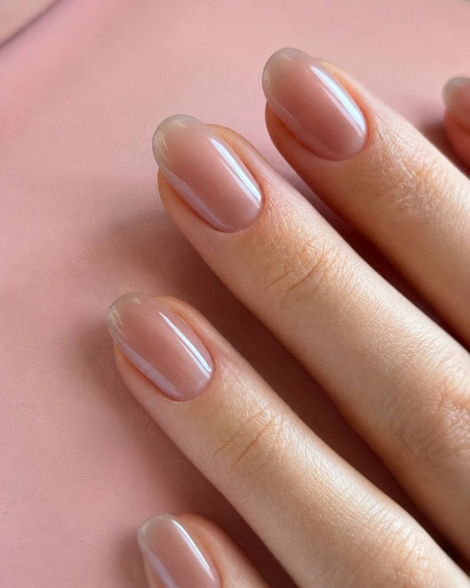 Glazed natural manicure with a sheer blush finish, resting on rose leather